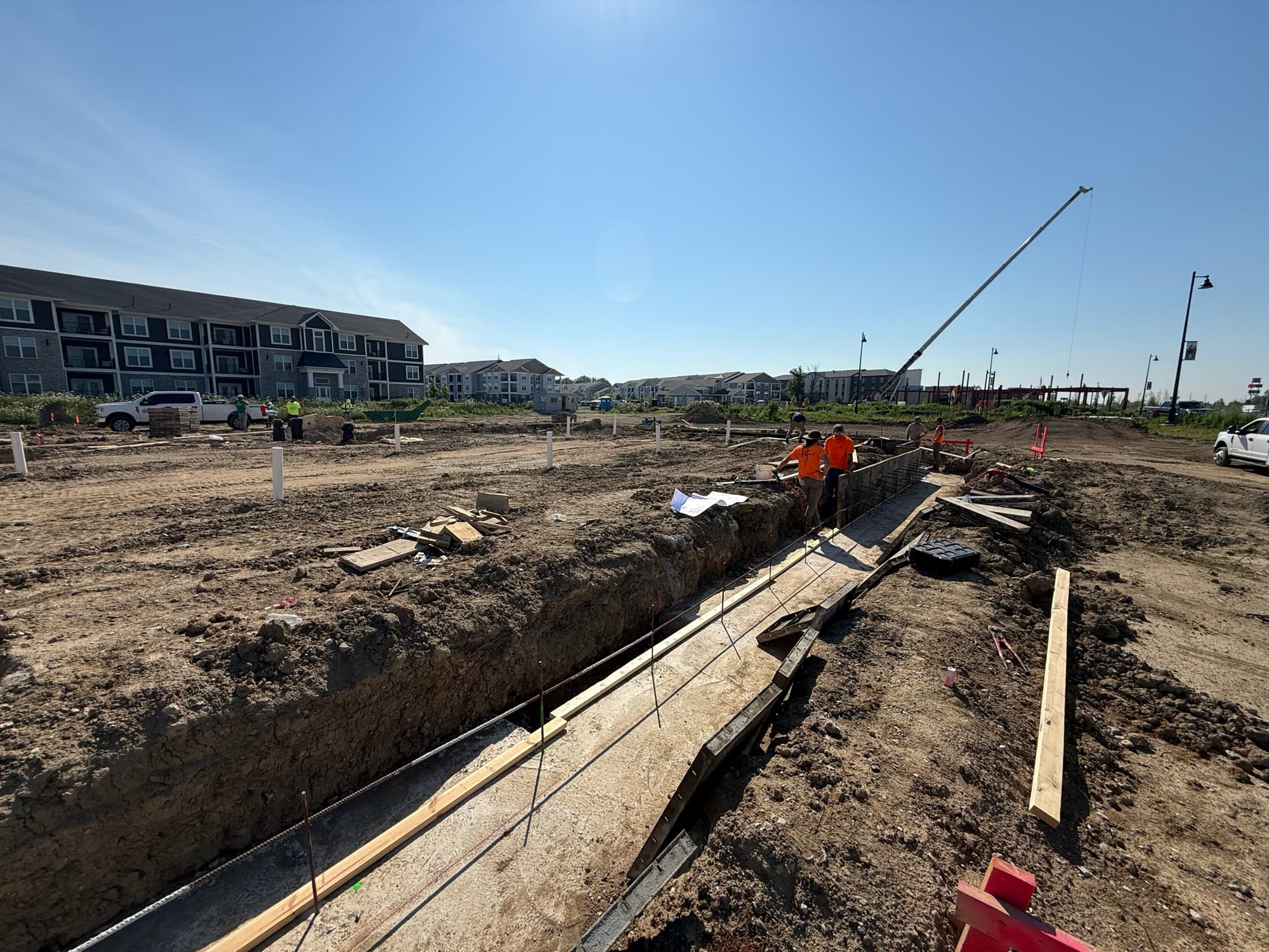 FT crew forming and pouring commercial footings beside a crane at a multifamily development