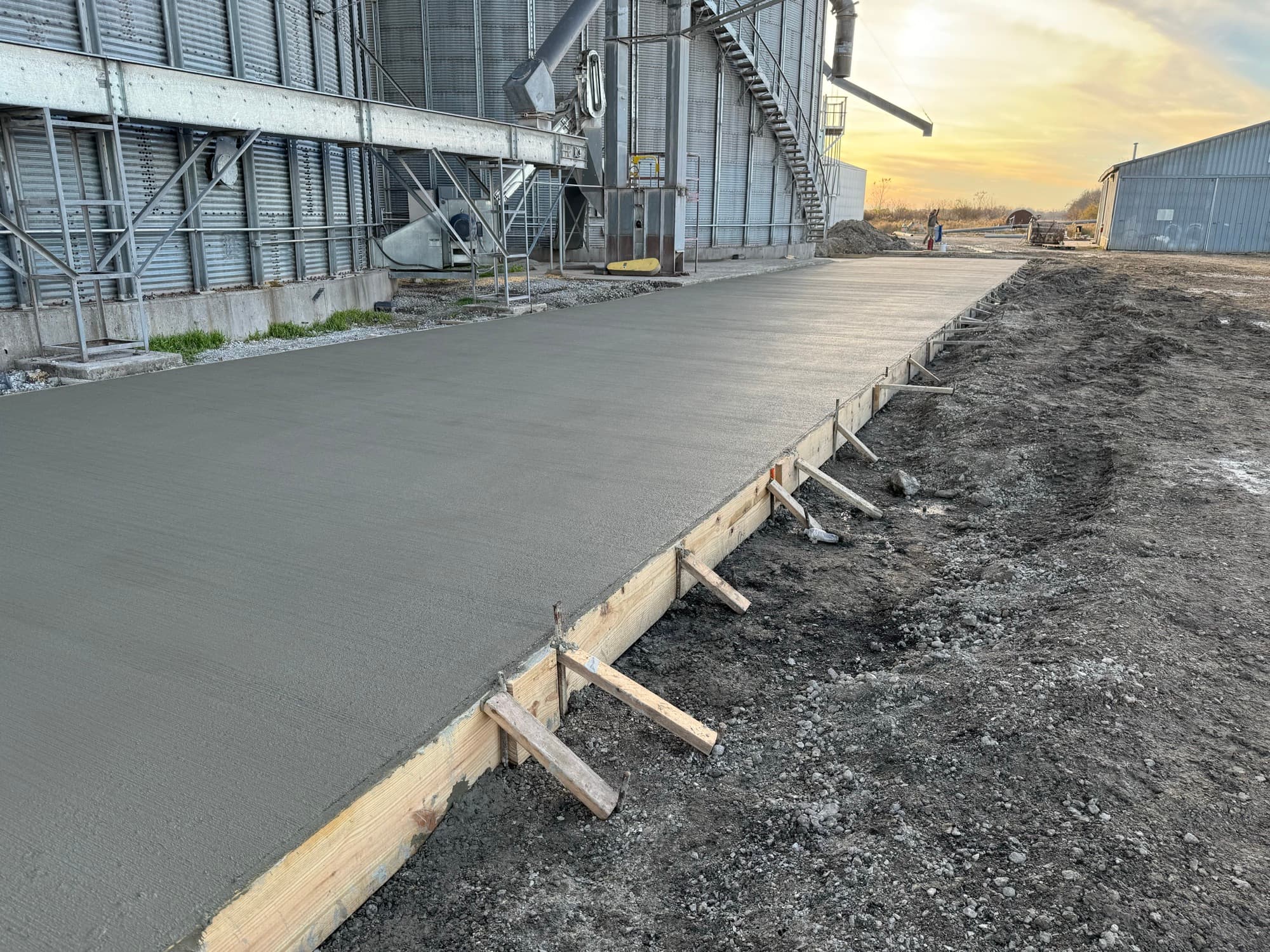 Broom-finished concrete pad running alongside grain silos at dusk