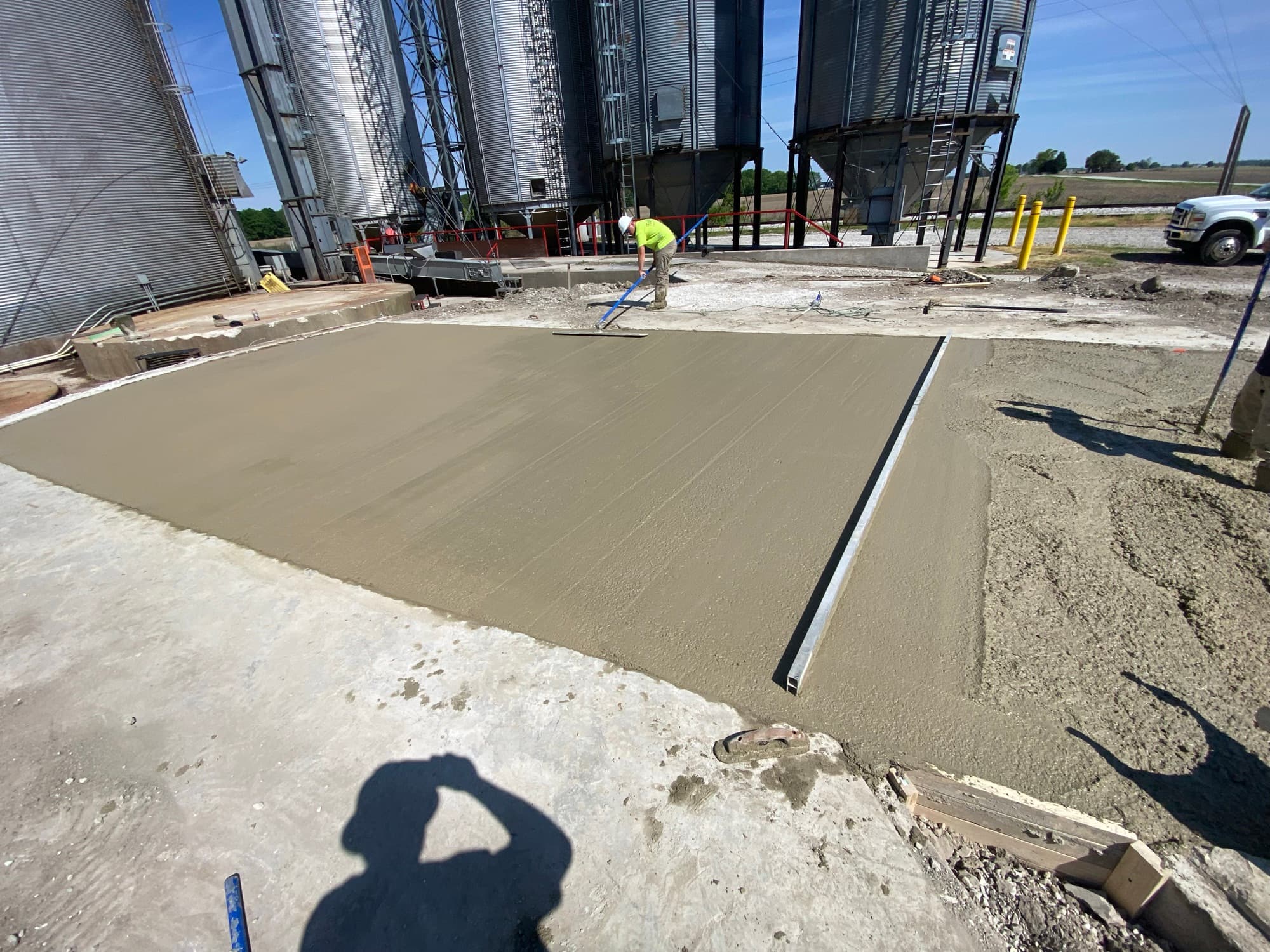 FT crew screeding a fresh concrete slab beside grain bins
